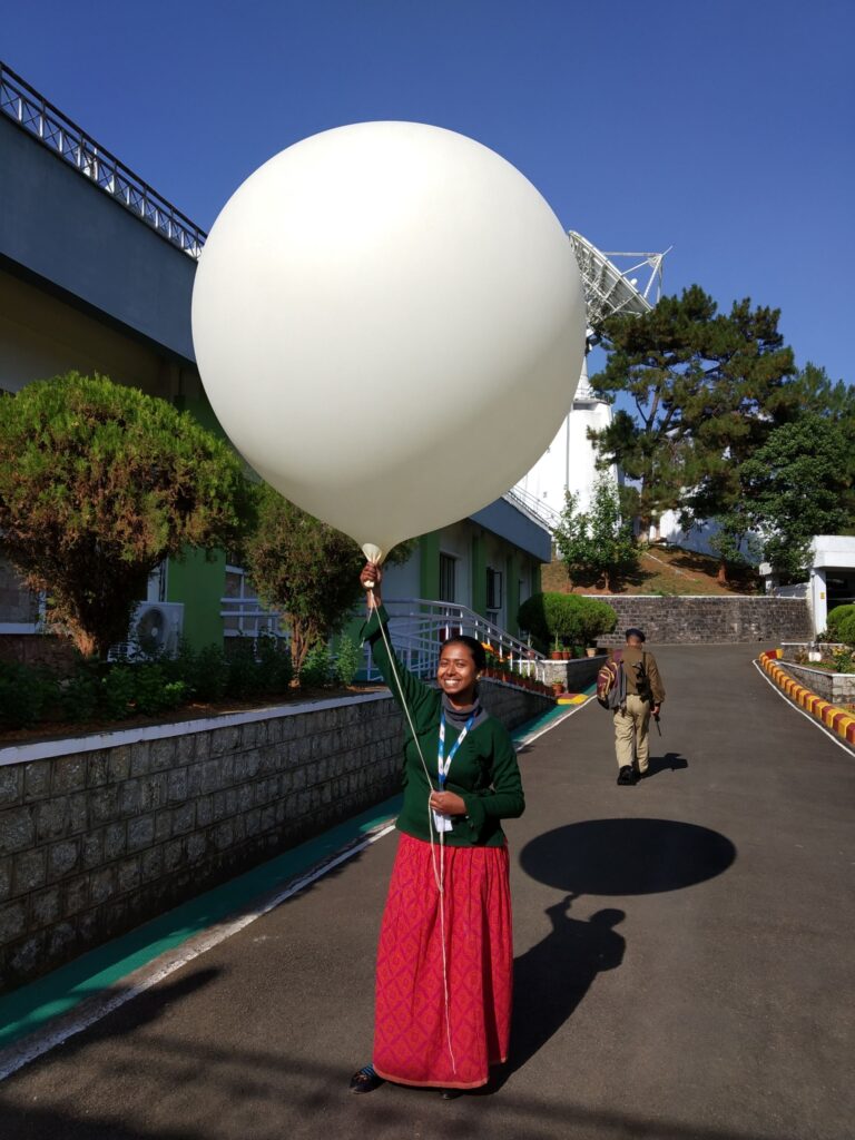 A woman in India holding a weather balloon and smiling into the camera