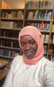 A Sudanese woman smiling into the camera in front of library shelves