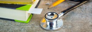 A close up for a stethoscope on a desk, alongside some books and a yellow pencil