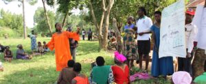 Students from African Rural University, Uganda, holding up posters and explaining things to community members outside on the grass